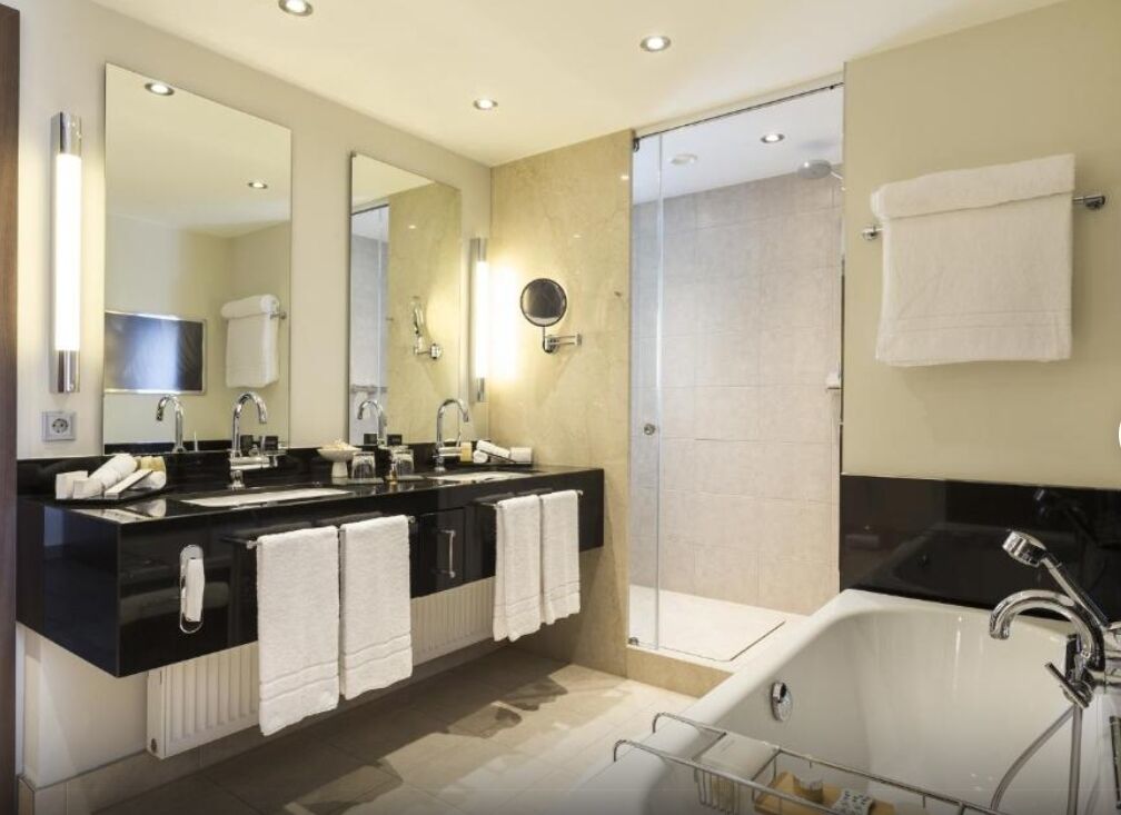 A modern bathroom with a black countertop, two sinks, a large mirror, a bathtub, and a glass shower enclosure.