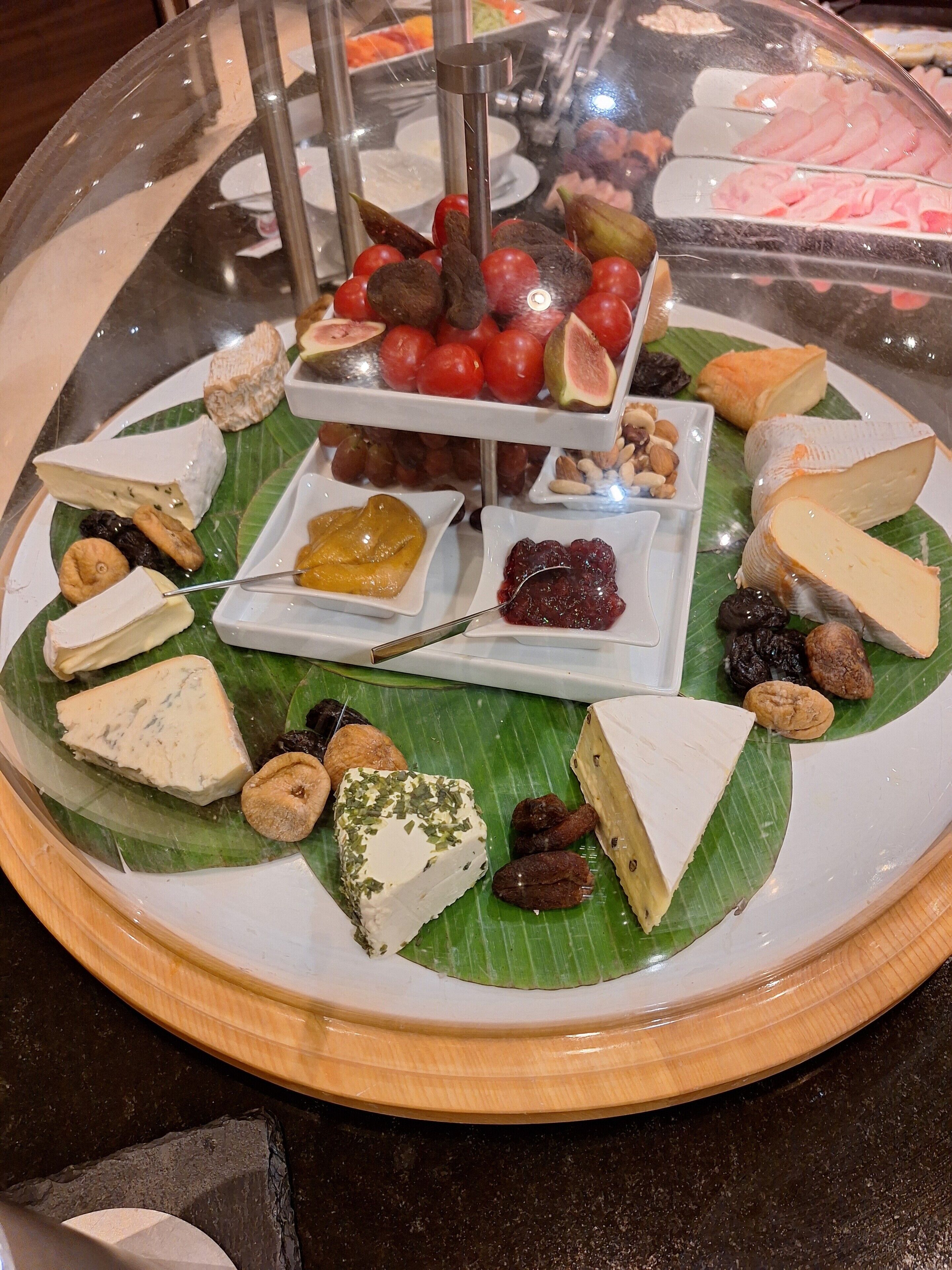 A cheese board with various cheeses, fruits, and nuts on a banana leaf.