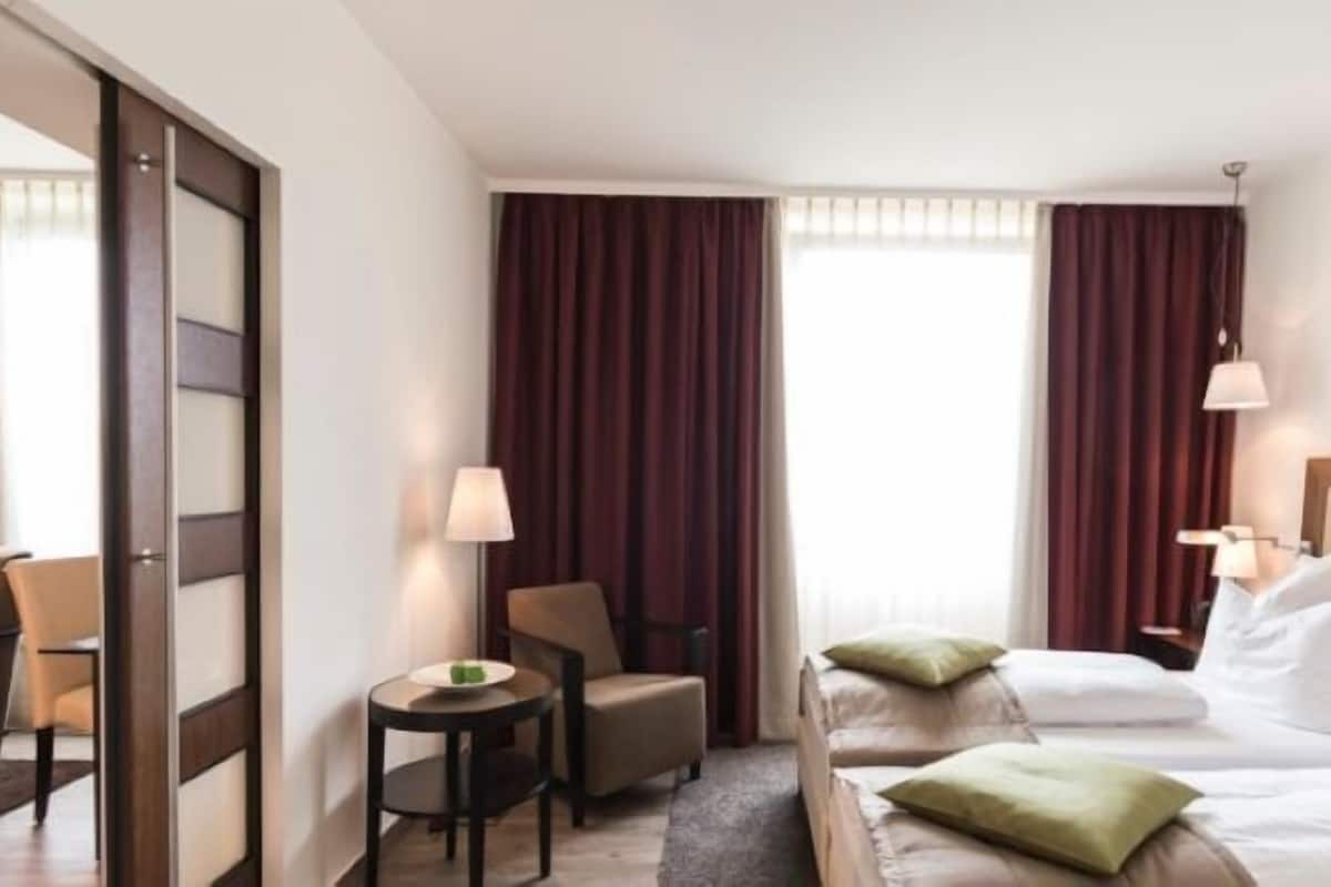 A hotel room with a bed, two chairs, a small table, and a window with curtains.