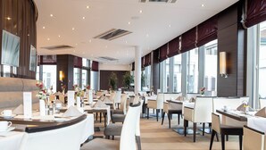 A modern restaurant with a long counter, multiple tables, and chairs.
