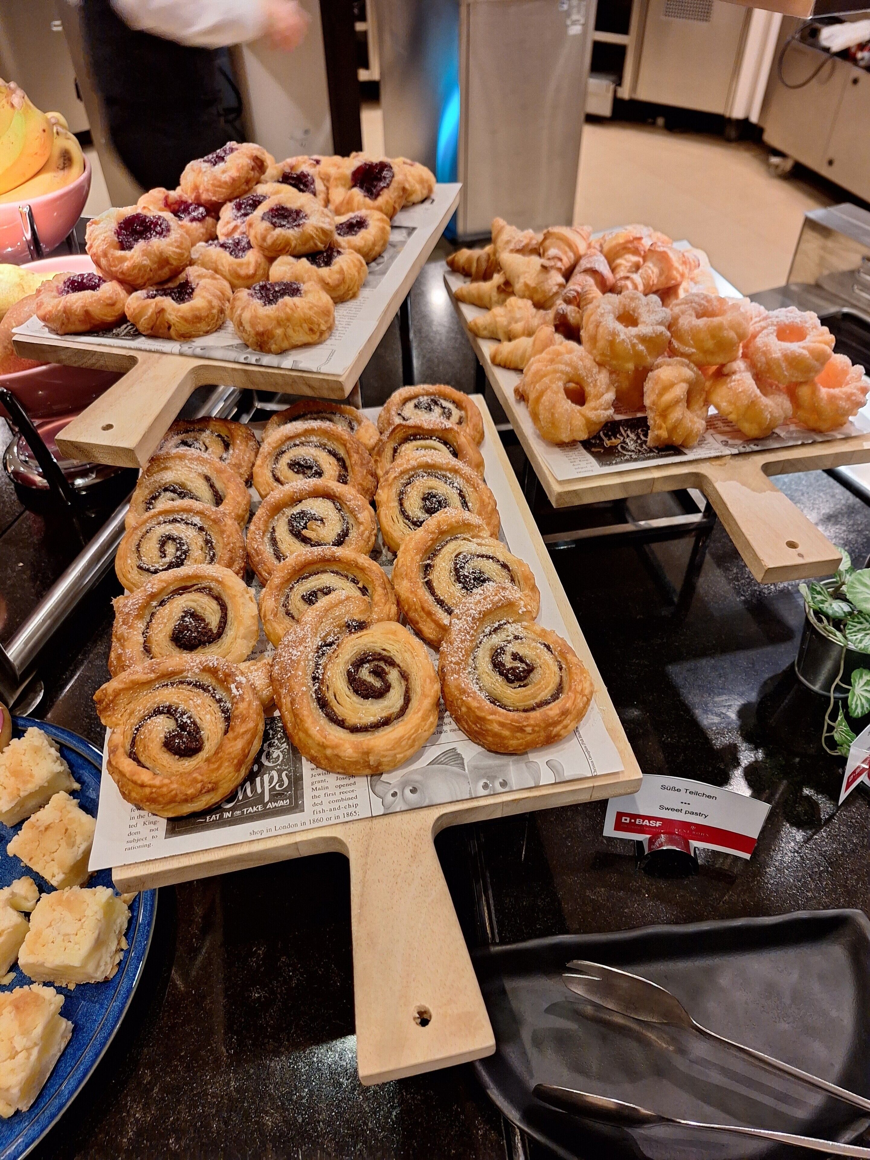 A buffet table with various pastries and desserts, including cinnamon rolls and croissants.