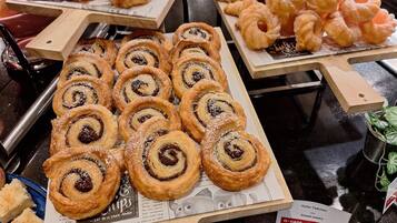 Une table de buffet proposant une variété de viennoiseries et de desserts, notamment des brioches à la cannelle et des croissants.