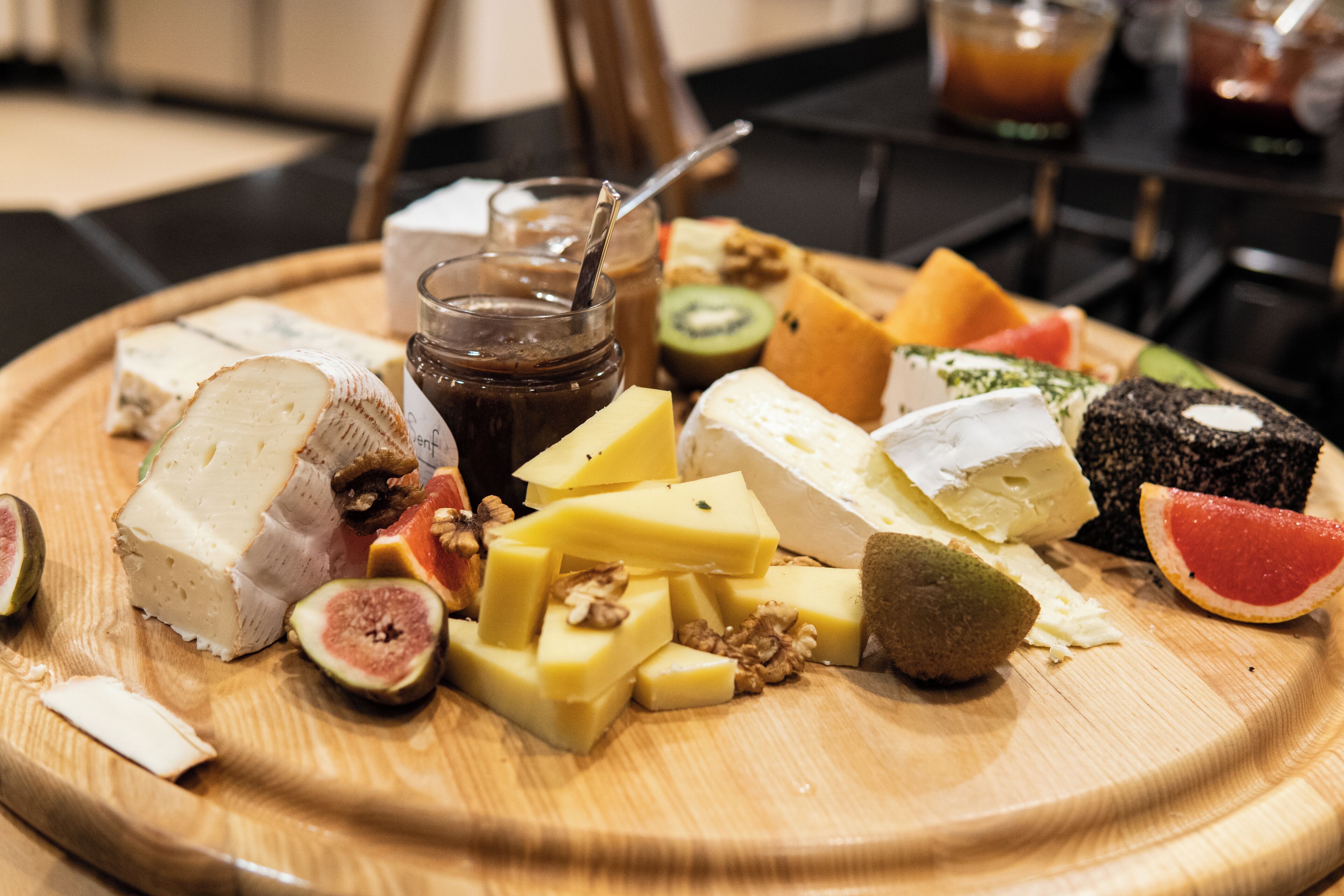Uma tábua de madeira com diversos queijos, frutas e um pote de creme de chocolate.