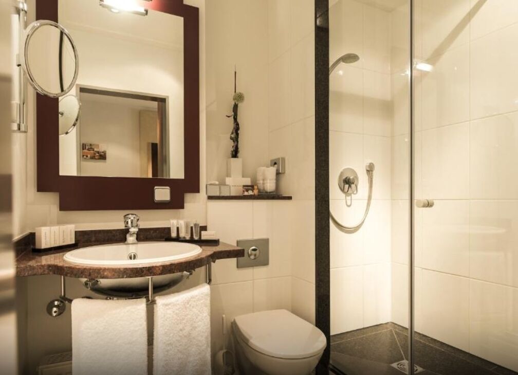Un bany modern amb rentaplat, mirall, vàter i dutxa amb portes de vidre.