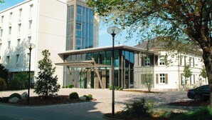 A modern building with a glass entrance, a covered walkway, and a parking area with a car.