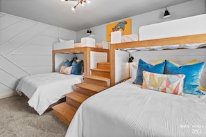 A bedroom with bunk beds, a wooden staircase, and a wall-mounted shelf.
