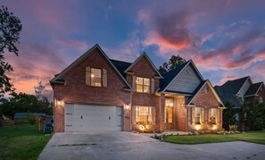 A two-story brick house with a garage, a covered front porch, and a well-maintained lawn.
