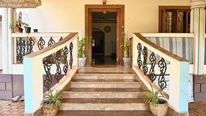 A staircase with ornate metal railings leading to a wooden door. There are potted plants at the base of the stairs. - Dragonfly Goa (Arambol)