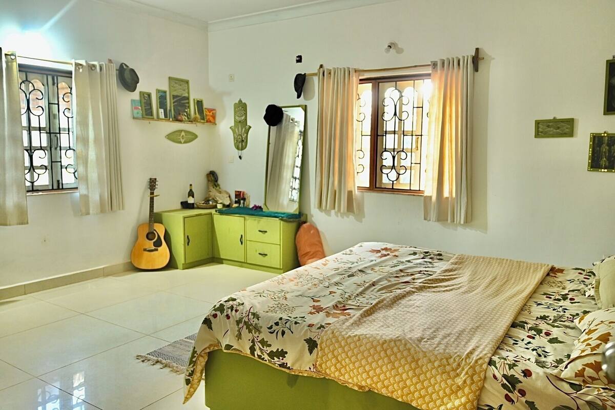 A bedroom with a bed, a dresser, a guitar, and a window with curtains.
