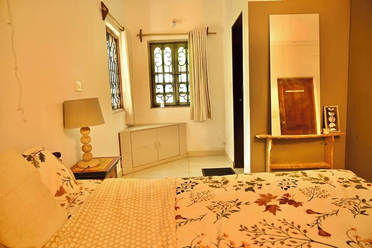 A bedroom with a bed, a nightstand, a window with curtains, a wardrobe, and a door.