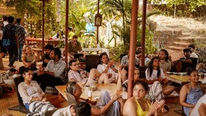 A group of people seated in an outdoor setting with tables and chairs, surrounded by greenery. - Dragonfly Goa (Arambol)