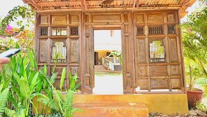 A wooden structure with a thatched roof, possibly a gazebo or entrance, surrounded by lush greenery. - Dragonfly Goa (Arambol)