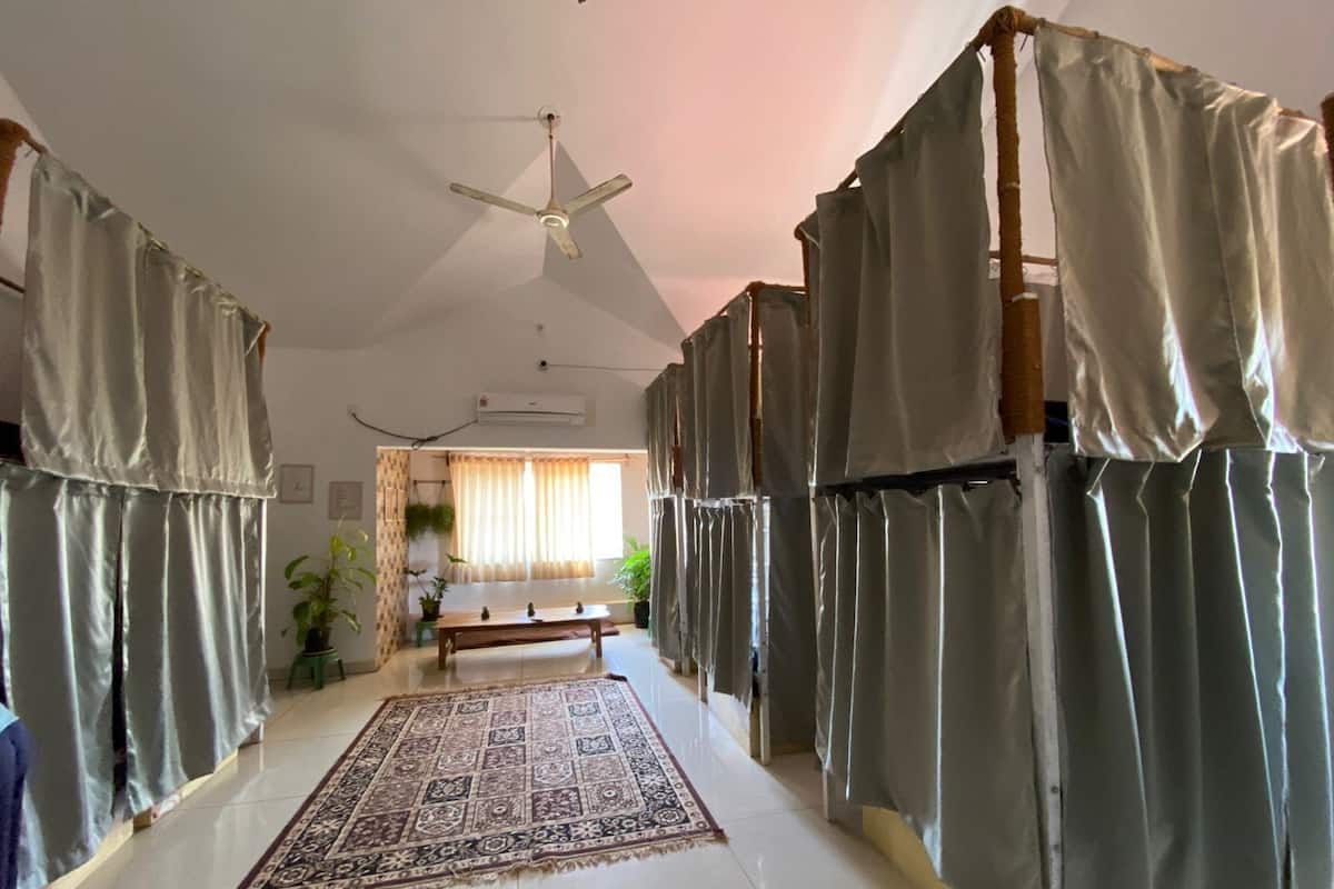 A room with a ceiling fan, a large window with curtains, a patterned rug, and a bed with curtains.