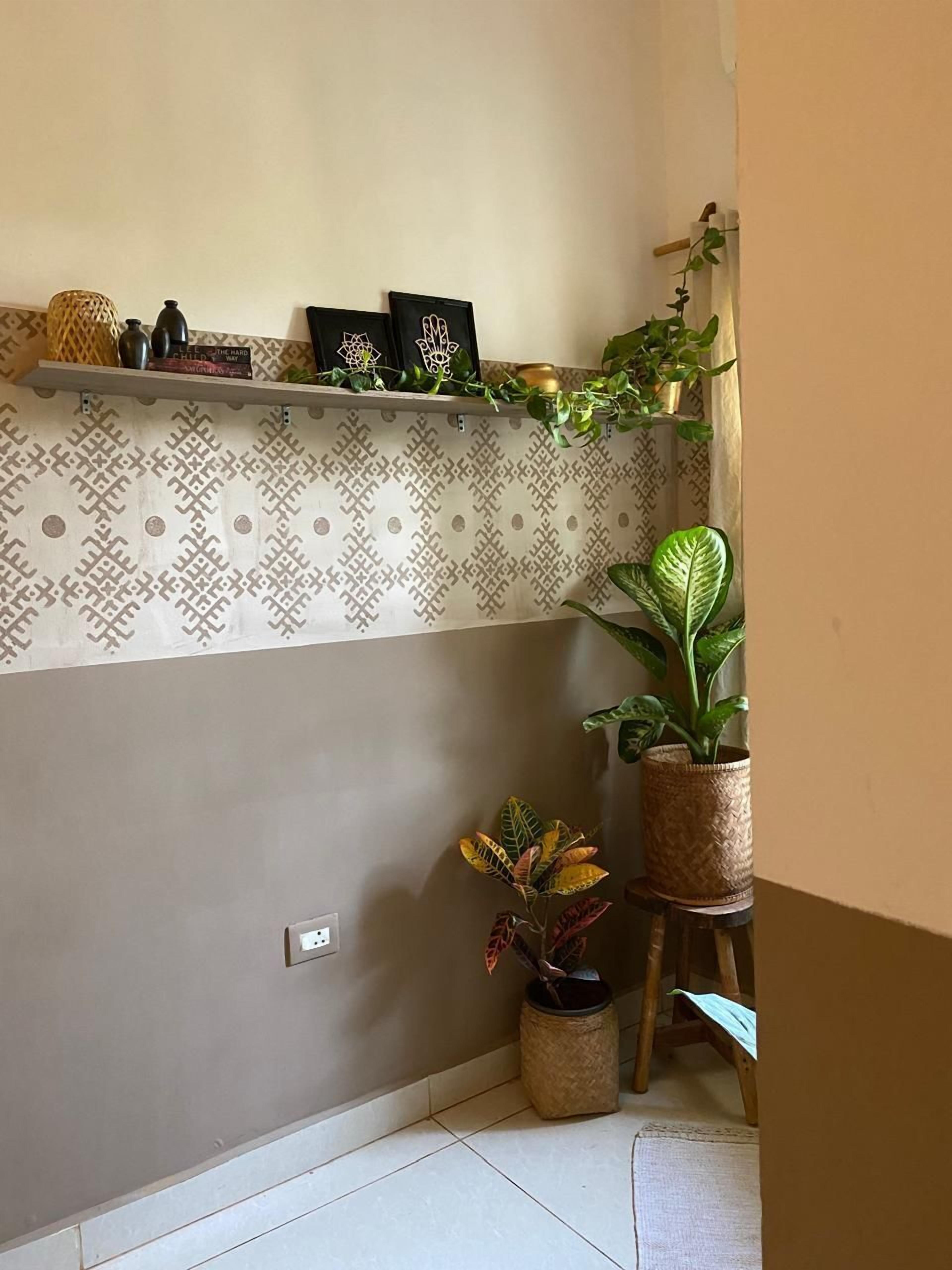 Un coin de pièce avec un mur orné de motifs, une étagère avec des objets décoratifs et des plantes en pot.