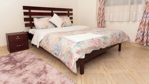 Een slaapkamer met een houten bed, een nachtkastje, een zacht tapijt en gordijnen met een patroon.