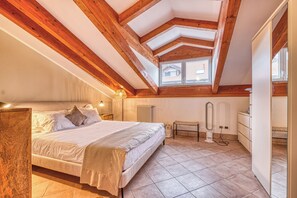 Une chambre avec un grand lit, des poutres en bois, un radiateur, un banc et une commode.