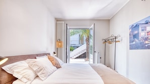 Ein Schlafzimmer mit einem großen Bett, einem Nachttisch, einer Lampe, Blick auf eine Treppe, die nach draußen führt, und einem an der Wand befestigten Wäscheständer.