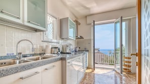 Eine moderne Küche mit Granit Arbeitsplatte, Edelstahlspüle und Meerblick durch eine offene Tür.