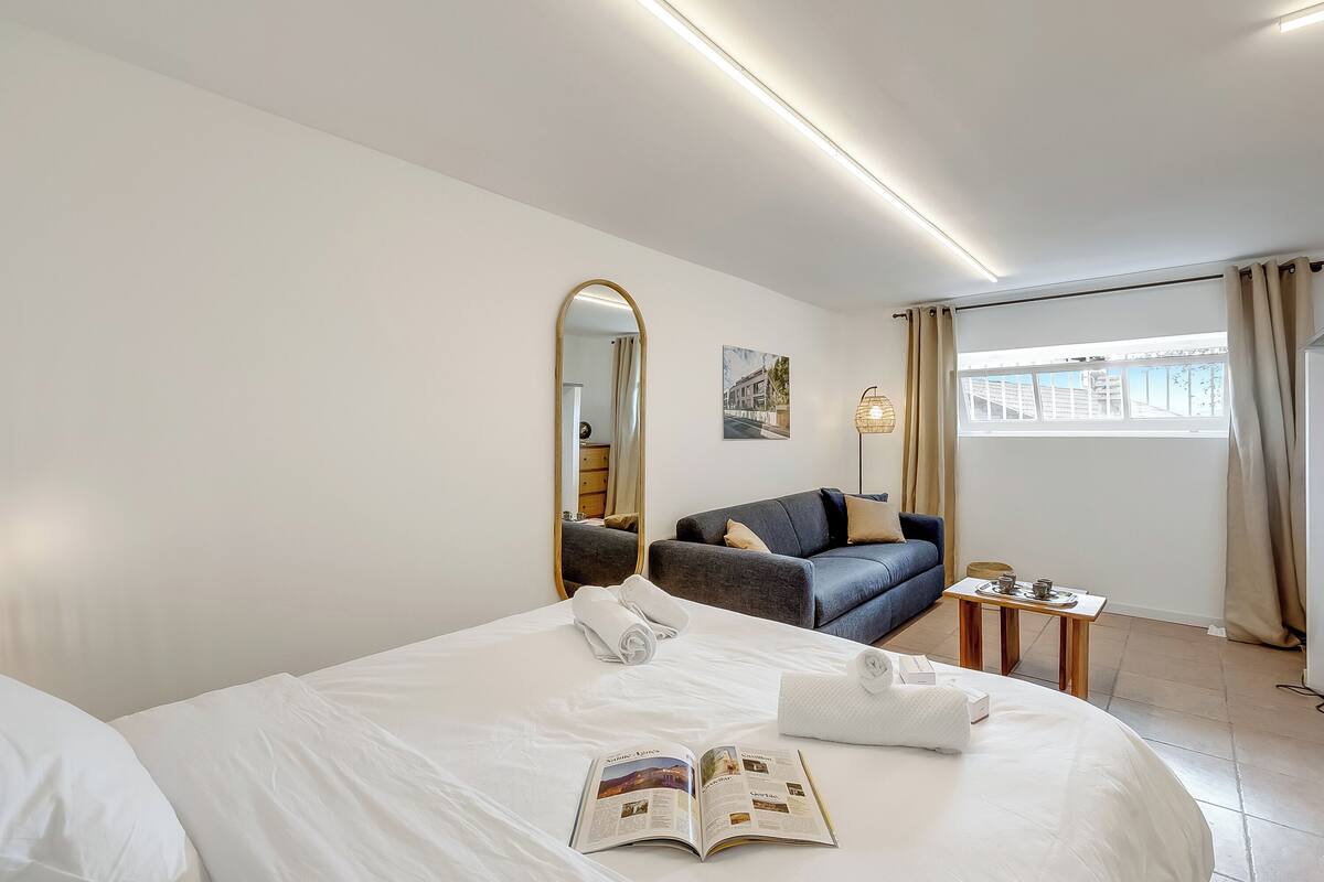 Une chambre d’hôtel avec un grand lit, un canapé, une petite table, un miroir et une fenêtre avec des rideaux.