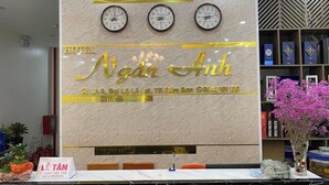 Un comptoir d’accueil d’hôtel avec un mur en marbre, trois horloges et une enseigne indiquant le nom et l’adresse de l’hôtel.