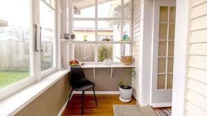 A sunlit corner with a black chair, a potted plant, and a shelf with various items.