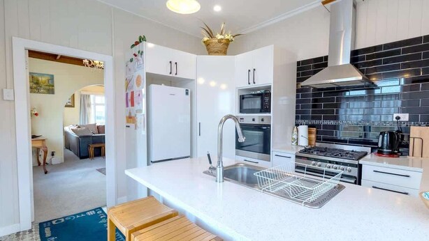 A modern kitchen with white cabinets, a black backsplash, stainless steel appliances, and a central island with a sink and stools.