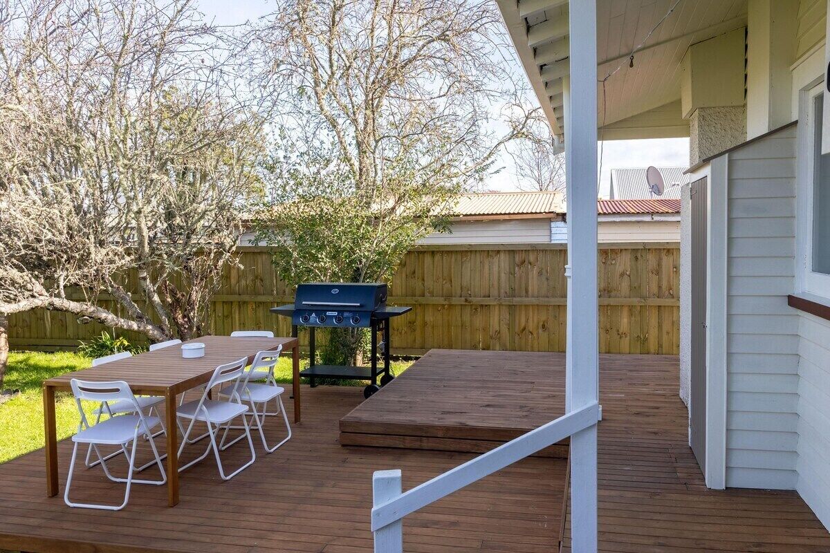 A wooden deck with a barbecue grill, a dining table with chairs, and a covered area.