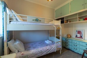 A bunk bed room with a lower bunk, a dresser with drawers, and a shelf with various items.