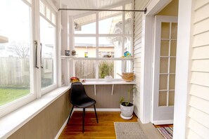 A sunlit room with a window, a chair, a shelf with items, and a potted plant.
