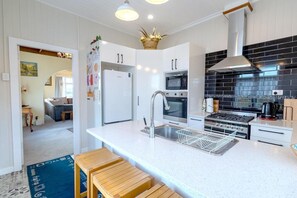 A modern kitchen with white cabinetry, a stainless steel sink, a black tiled backsplash, and a gas stove.