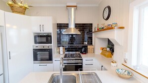 A modern kitchen with white cabinetry, stainless steel appliances, and a black tiled backsplash. - Central Villa - Character Home, Walk to CBD (Rotorua)