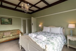 A bedroom with a bed, bedside tables, a chandelier, a couch, and a painting on the wall.