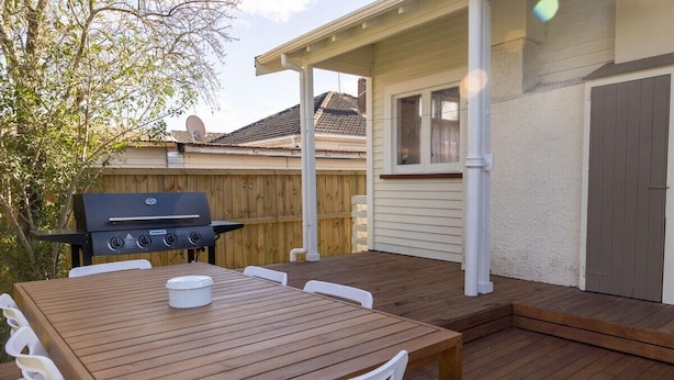 An outdoor patio with a wooden table and chairs, a barbecue grill, and a wooden fence. - Central Villa - Character Home, Walk to CBD (Rotorua)