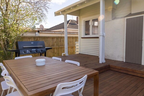An outdoor patio with a wooden table and chairs, a barbecue grill, and a wooden fence.