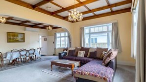 A spacious living room with a large sofa, a dining table with chairs, and a chandelier.