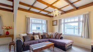 A living room with a sectional sofa, a wooden coffee table, and a chandelier. - Central Villa - Character Home, Walk to CBD (Rotorua)