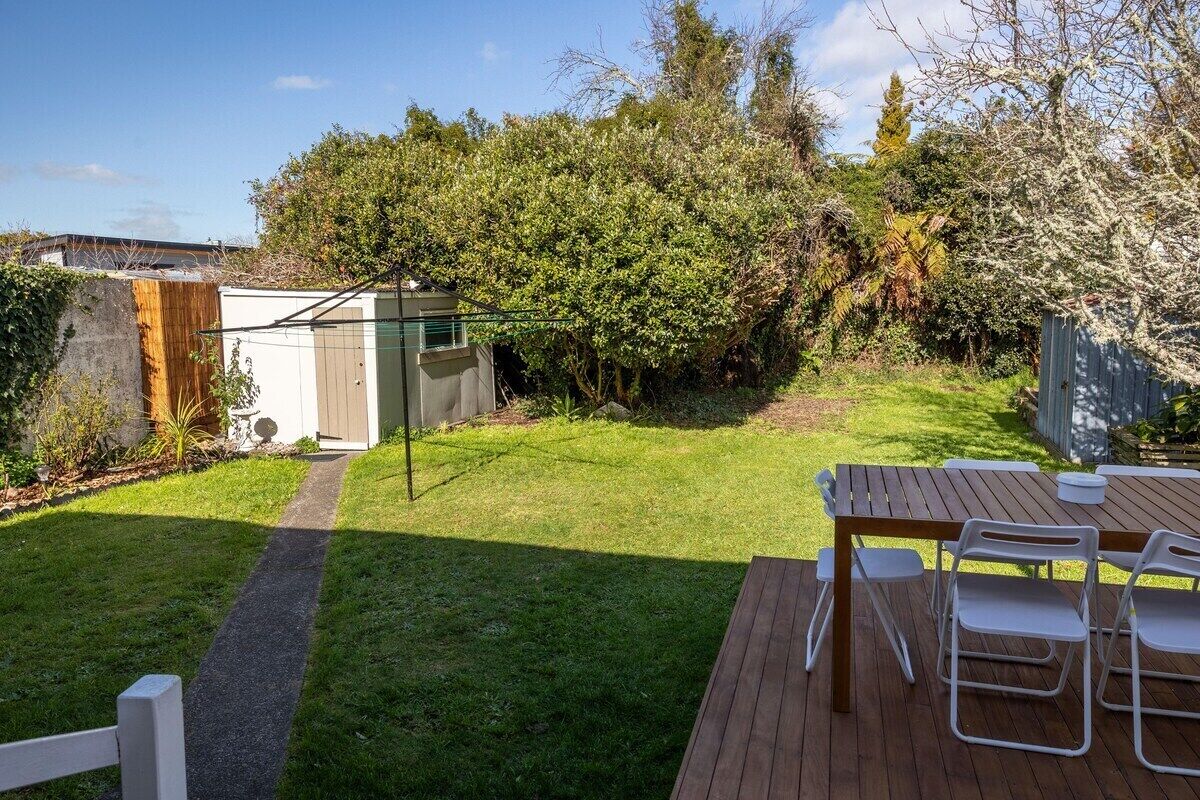 A backyard with a wooden deck, a table with chairs, and a white shed.