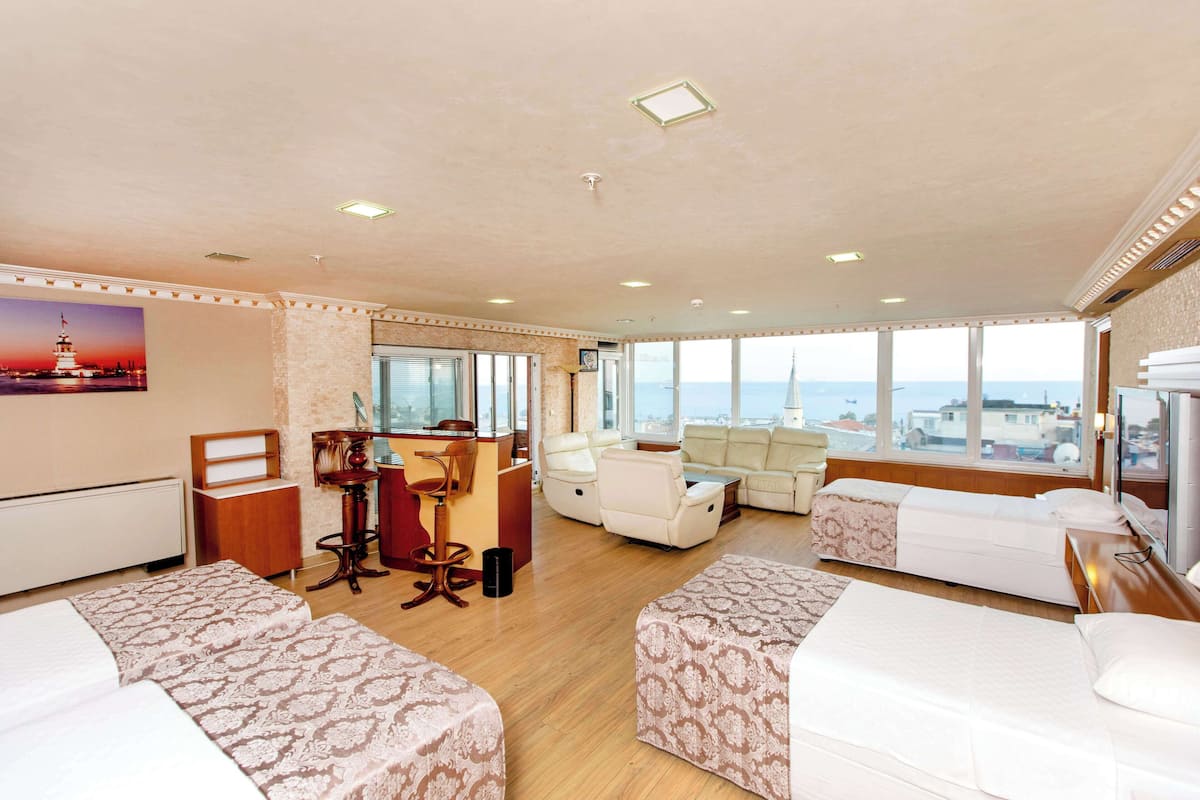A hotel room with two beds, a desk, a sofa, and a large window with a city view.
