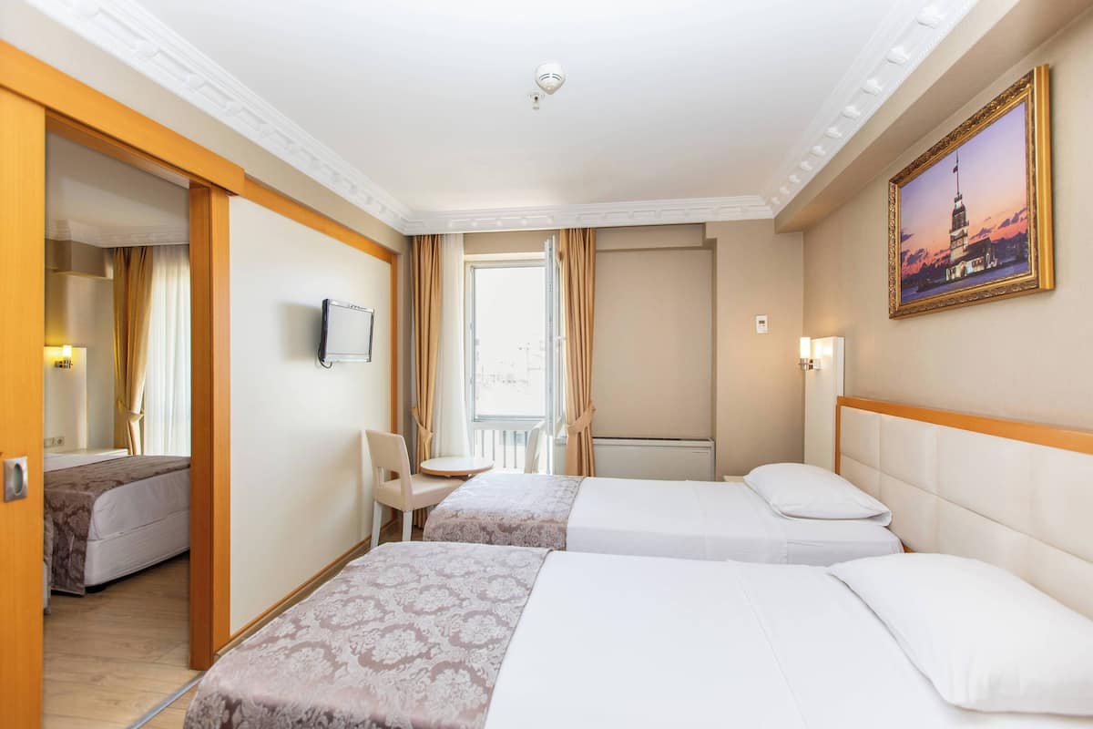 A hotel room with two beds, a TV, a desk, and a window with curtains.