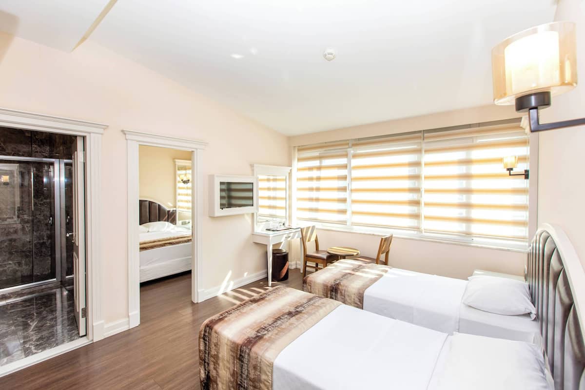 A hotel room with two beds, a desk, a chair, and a shower area.
