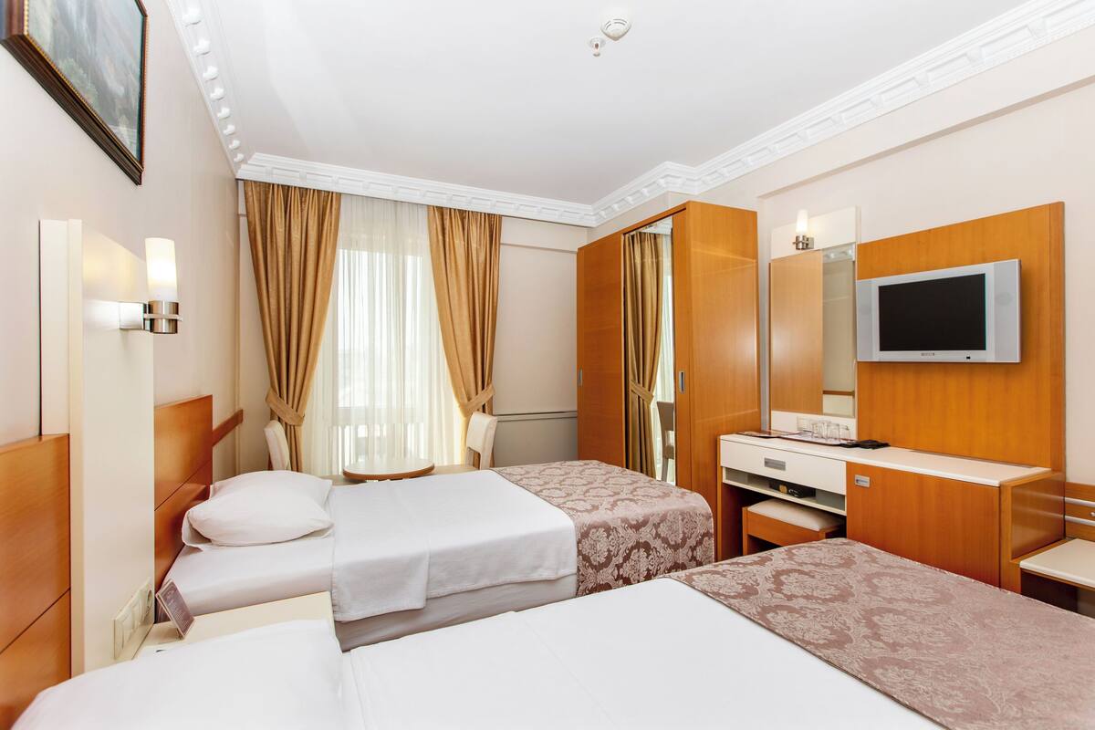 A hotel room with two beds, a desk, a television, and a mirror.