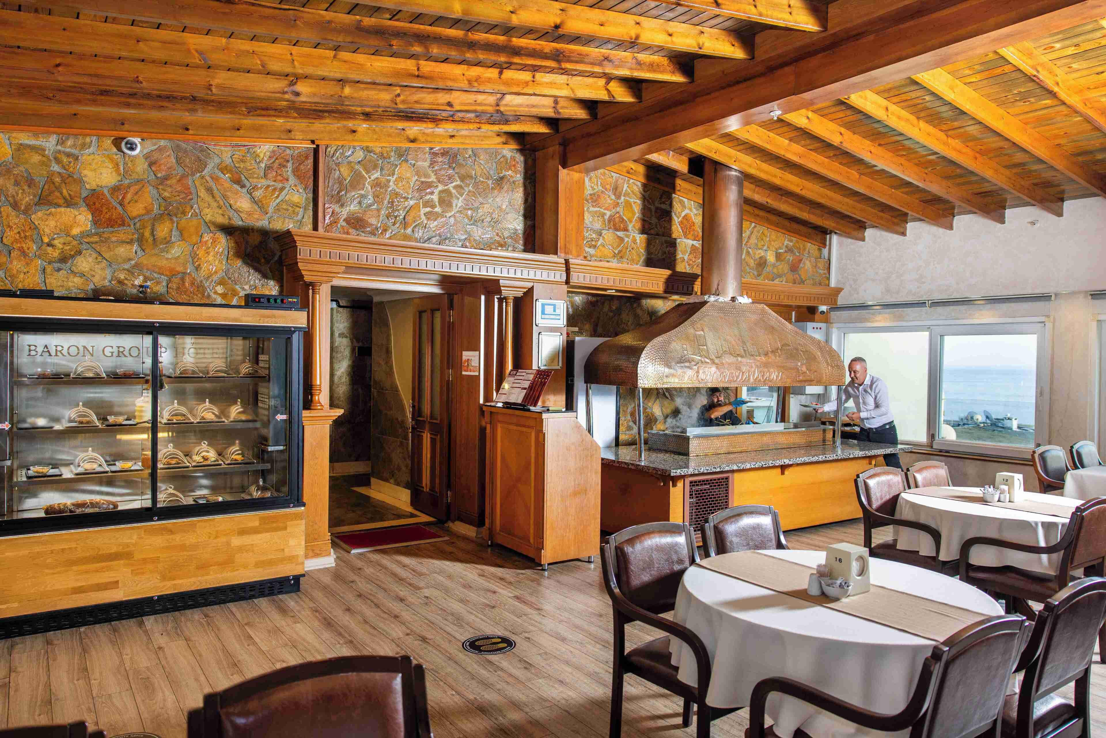 Een restaurant met houten balken, stenen muren en een stenen open haard. Er staan tafels en stoelen voor het diner.