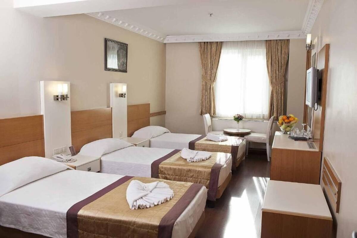A hotel room with three beds, a desk, a chair, a television, and a window with curtains.