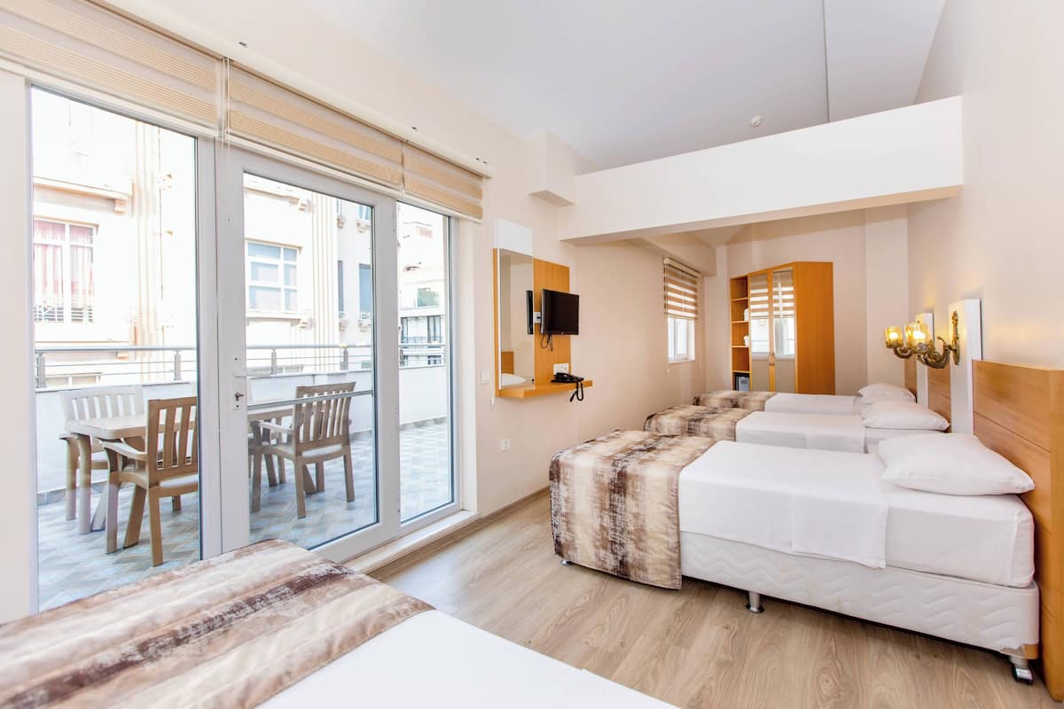 A hotel room with a large sliding glass door to a balcony, a bed with a wooden headboard, a bedside table, and a flat-screen TV mounted on the wall.