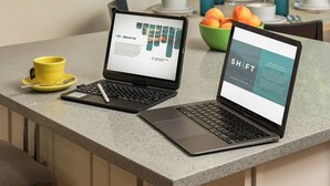 Deux ordinateurs portables sont posés sur un plan de travail de cuisine, à côté d’une tasse jaune et d’une cuillère.