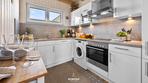 Une cuisine moderne avec des meubles blancs, un four encastré, un lave-linge et une machine à café.