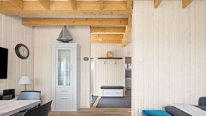 Un intérieur moderne avec un plafond en bois, un coin repas comprenant une table et des chaises, une cuisine en arrière-plan et un coin salon confortable avec un canapé.