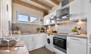 A modern kitchen with white cabinets, a built-in oven, a washing machine, and a coffee maker.