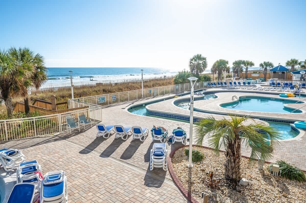 A pool area with lounge chairs and a view of the beach.