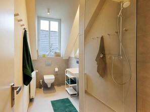 Ein modernes Badezimmer mit Toilette, Waschbecken und Dusche. Über der Toilette befindet sich ein Fenster und auf dem Boden liegt ein grüner Teppich.